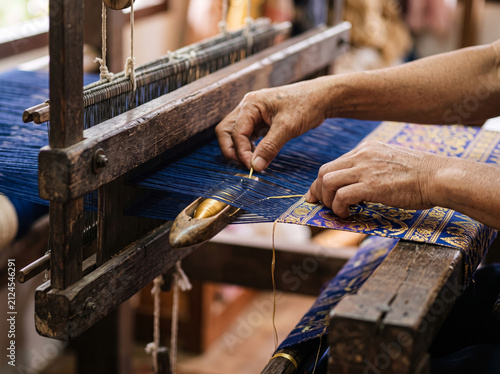 Naklejka Weaver operating traditional wooden handloom to weave textile fabric threads