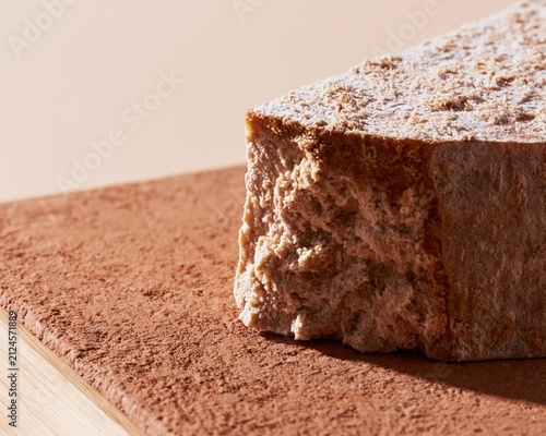 Artisan cheese with a powdery bloomy rind on a textured terracotta surface, showcasing a crumbly curd texture for gourmet food and dairy branding