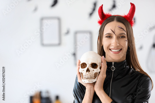 Beautiful young happy woman dressed as devil for Halloween with human skull a...