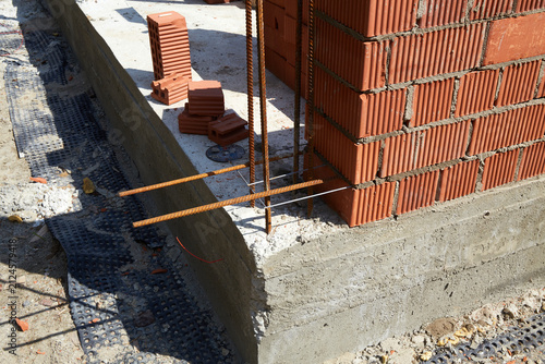 Принти на полотні A construction site features a newly built brick wall with visible rebar bars extending from the concrete foundation