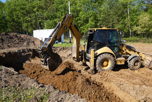 Backhoe loader digging and moving soil in a trench at a construction site, shaping the ground for foundation