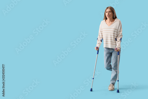 Injured young woman after accident with crutches on blue background