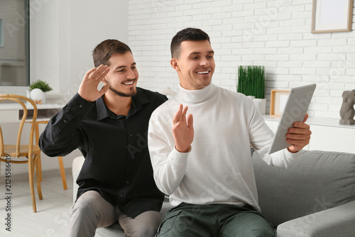 Young men with tablet computer video chatting on online date at home