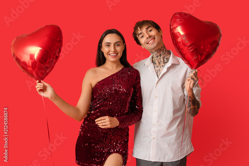 Young couple with air balloons in shape of heart on red background. Valentine...