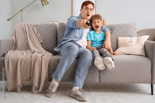Shocked little boy with his father watching TV at home