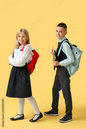 Cute pupils with backpacks on yellow background