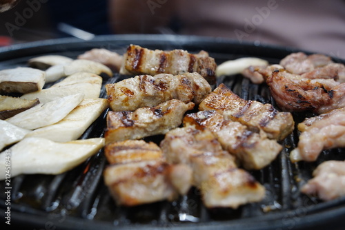 Thick pork belly slices and mushrooms grilling on a charcoal BBQ grill