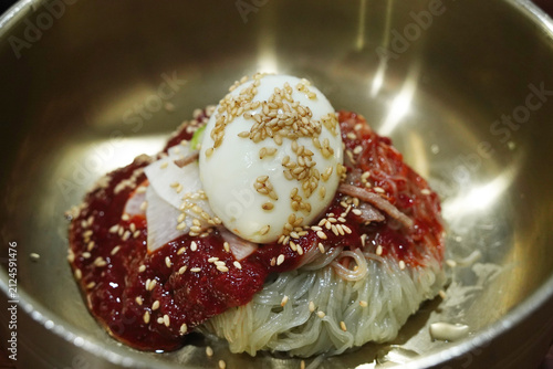 Spicy cold buckwheat noodles Bibim-Naengmyeon with red sauce and egg in brass bowl