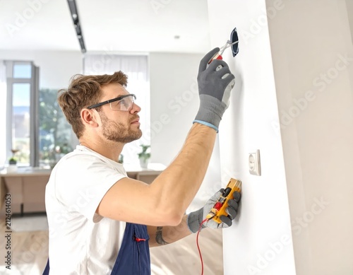 Electrician testing wall outlet using digital multimeter.