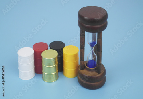 Different crude oil barrels and hourglass on blue background.