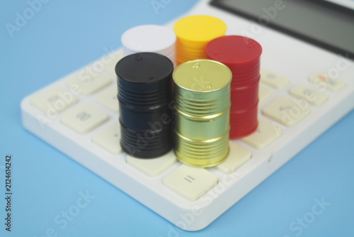 Different crude oil barrels on calculator on blue background. Crude oil price concept.