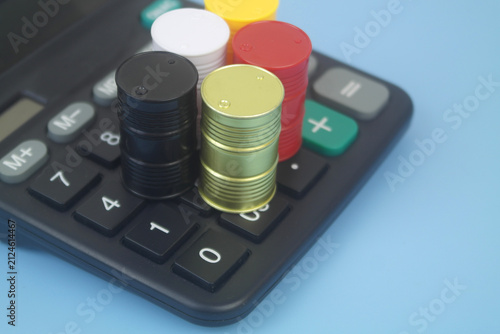 Different crude oil barrels on calculator on blue background. Crude oil price concept.