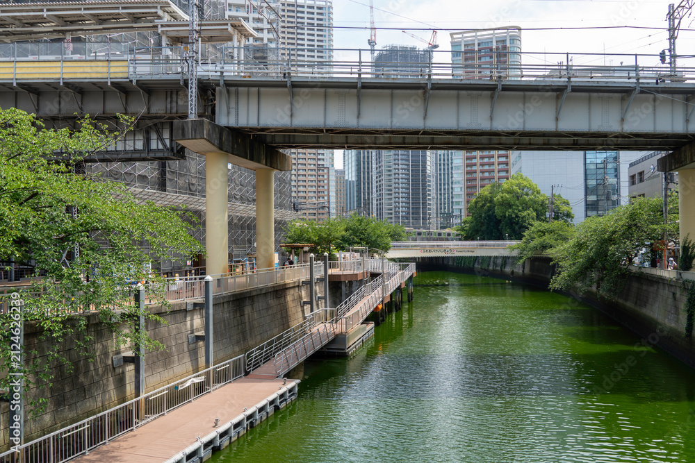 Fototapeta premium Scenic view of a riverside walkway along an urban canal with elevated bridges and buildings