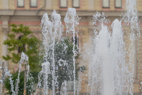 Spray of water from a fountain in a city park during the day with historic buildings in the background