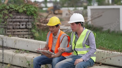Two Civil Engineers in Hard Hats and Safety Vests Inspecting Construction Site with Blueprint