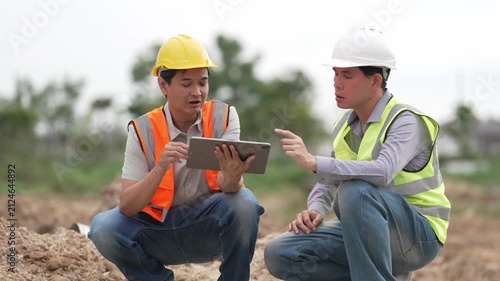 Two Civil Engineers in Hard Hats and Safety Vests Inspecting Construction Site with Blueprint