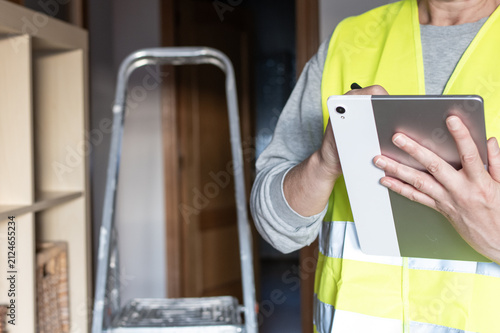 Property inspector wearing a reflective safety vest holding a digital tablet with a stylus. Diligently recording notes and conducting a thorough assessment of a residential home