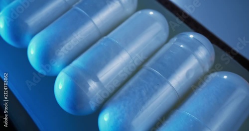 Tracking shot of translucent capsules sliding across blister pack on conveyor belt in production, macro probe lens.