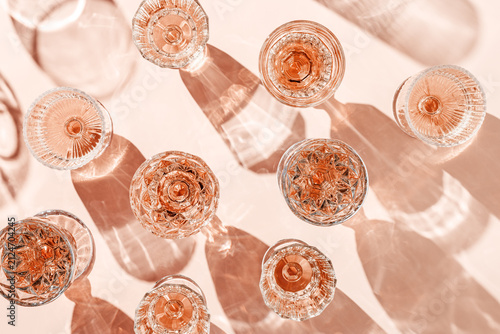 Stylish flat lay of rose wine crystal glasses casting shadows on pastel peach background. Minimal Top view sparkling alcohol drinking, champagne drinks at sun, wine aesthetic party concept