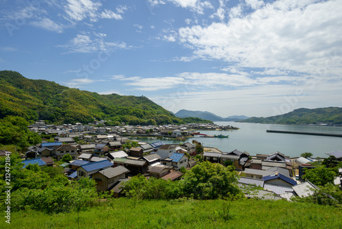 Scenic landscape view of a coastal town with traditional tiled roofs, tranquil bay, green mountains, and blue sky with clouds in the Seto Inland Sea, Japan
