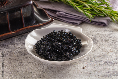 Canvas Print Black caviar in white ceramic bowl with rosemary and dark tray on textured surfa