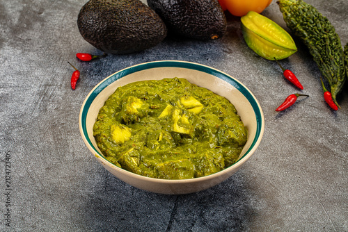 Obraz na plátně Green paneer curry with spinach in ceramic bowl surrounded by avocados red chili