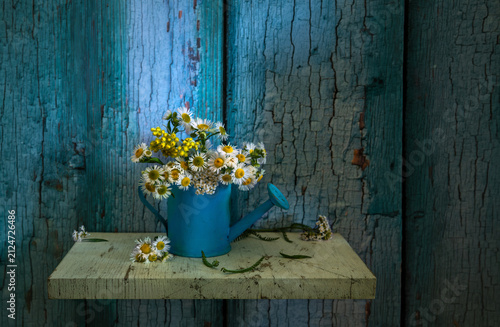 A small bouquet of meadow daisies in a blue watering can on a dark background.