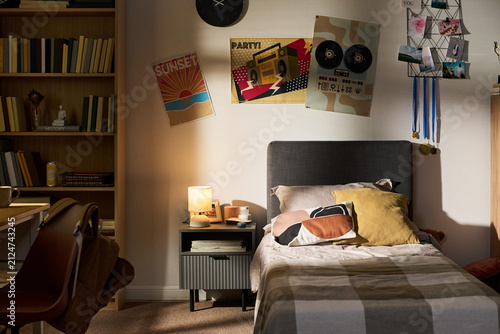 Empty teenager bedroom showing single bed, nightstand with lamp, and posters on wall. Image suitable for youth lifestyle marketing, interior design inspiration, or real estate staging