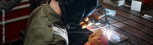Картината върху платно Young adult Caucasian male welder in protective mask welding metal with colleague in workshop, representing teamwork