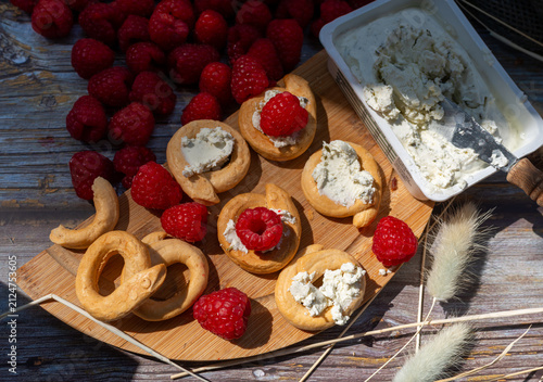 Foto Crisp ring-shaped crackers served with herb cream cheese and ripe red raspberries, Rubus idaeus, on a wooden board