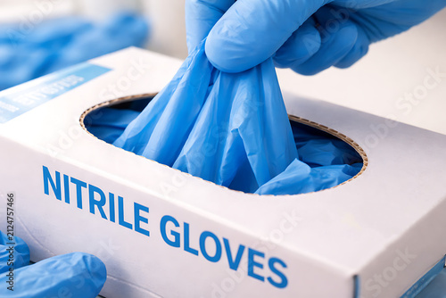 Gloved hands removing blue nitrile gloves from box in medical workplace closeup