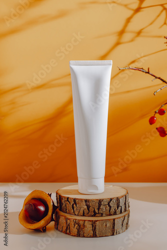 Bottle of mockup facial cream on wooden podium with autumn decorations on orange background with aesthetic shadows