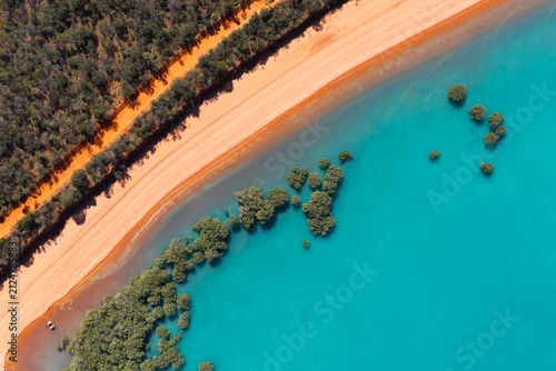 Aerial view of trees in ocean along red sandy coastline with turquoise water at Red Sand Beach, Roebuck Bay, Broome, Western Australia
