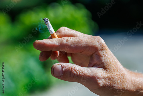 Man's hand holding a burning cigarette with smoke close-up, smoking habit and tobacco concept