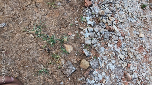 Canvas Print Contrast between dry cracked earth with sparse grass and a section of loose gravel and rocks
