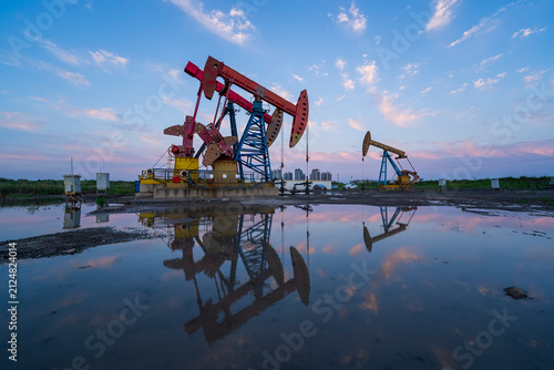 in the evening, oil pumps are running, The oil pump and the beautiful sunset reflected in the water, the silhouette of the beam pumping unit in the evening.