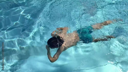 Child holding nose while swimming underwater in clear blue pool