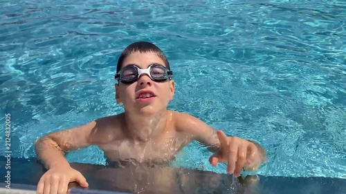 Smiling boy in goggles talking directly to camera in swimming pool