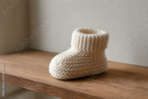 Knitted baby bootie resting on wooden shelf