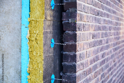 Cuadro en lienzo Detailed cross-section of a multi-layer cavity wall insulation system showing concrete, blue XPS board, mineral wool insulation, metal wall ties with blue retainers, and dark clinker brick cladding