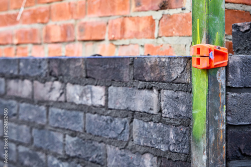 Cuadro en lienzo Close-up of an orange line block clamp on a metal corner profile holding a blue mason line for brickwork alignment on a dark clinker brick wall