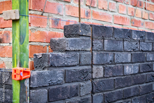 фотографія Dark clinker brick wall under construction showing stepped masonry, vertical expansion joint, and blue mason line attached to a green corner guide profile