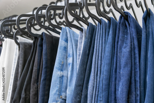 Collection of various denim pants hanging on black hangers, showcasing different shades and textures, emphasizing fashion trends and clothing organization in a retail environment