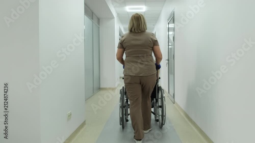 Healthcare worker transports disabled young woman in wheelchair for medical care. Patient mobility support and rehabilitation program