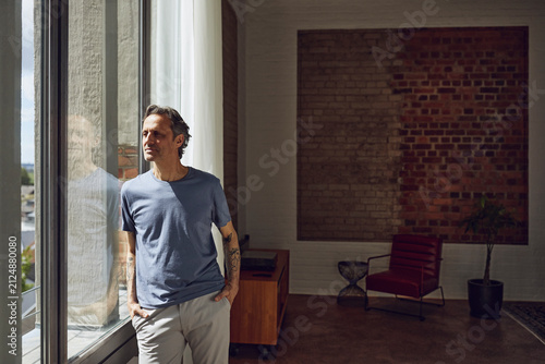 Senior man looking out of window in a loft flat