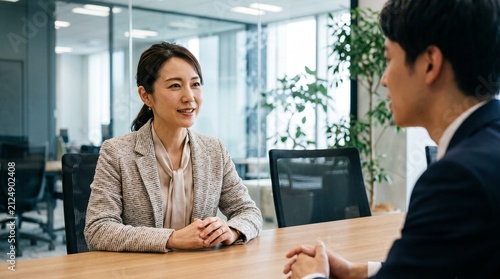 会議室の席に座り、テーブルの対面に座る部下に穏やかな笑顔で話しかけている30代日本人女性社員のクローズアップ