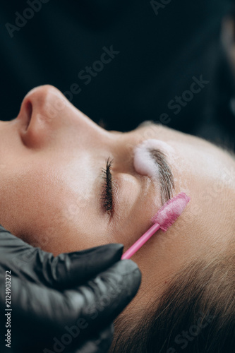 Close-up of a beauty specialist applying lamination solution to a clients eyebrow with a spoolie brush during a professional brow treatment.