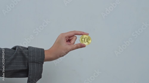 Businesswoman holds up shiny gold bitcoin coin against plain white background for symbolizing crypto assets