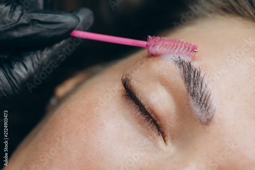 Close-up of a beauty specialist applying lamination solution to a clients eyebrow with a spoolie brush during a professional brow treatment.