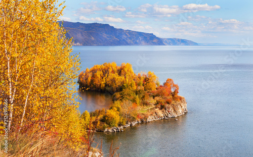 Autumn landscape of Baikal Lake. View from rocky shore with yellow birch trees to Cape Shamansky - natural landmark on September sunny day. Nature background. Outdoor recreation and travels